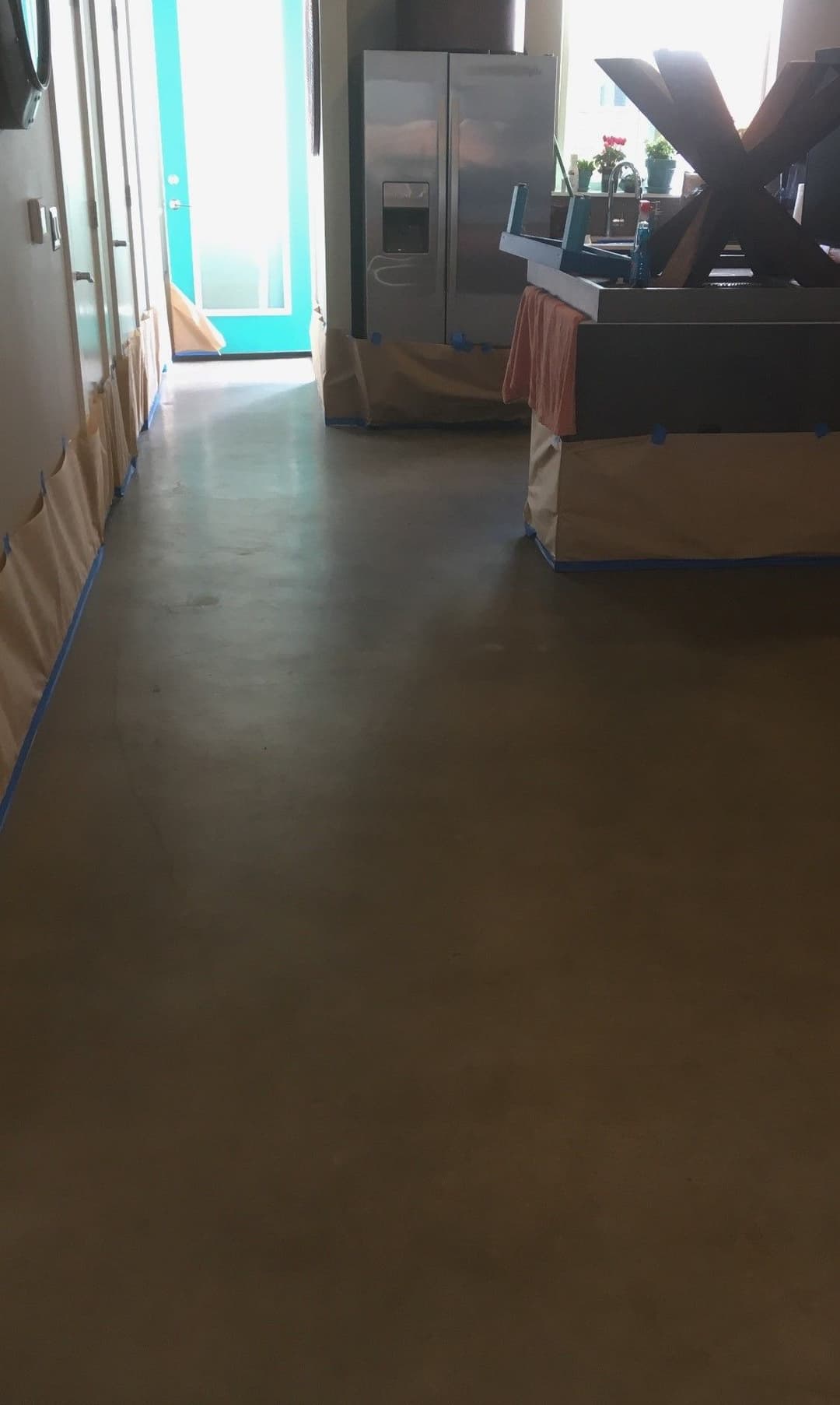 Renovated kitchen with polished concrete floor and blue painter's tape along the walls.
