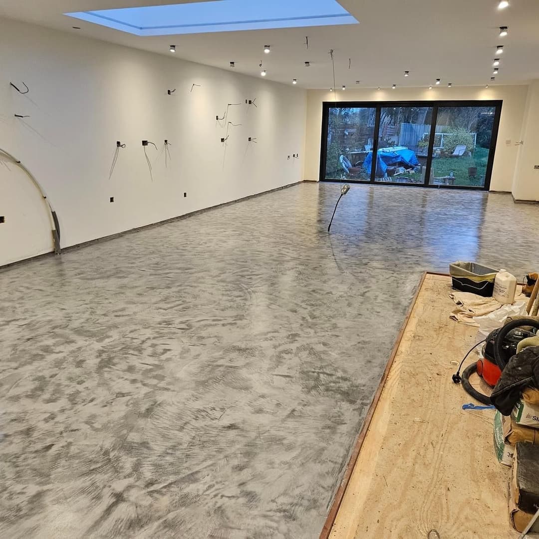 Modern interior space with polished concrete floor and large windows overlooking a garden.