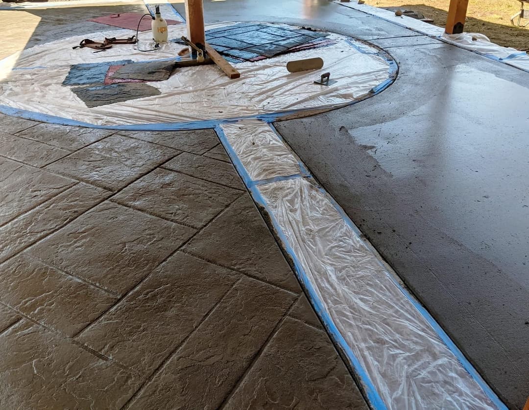 Stamped concrete patio installation with textured surface and protective sheeting.