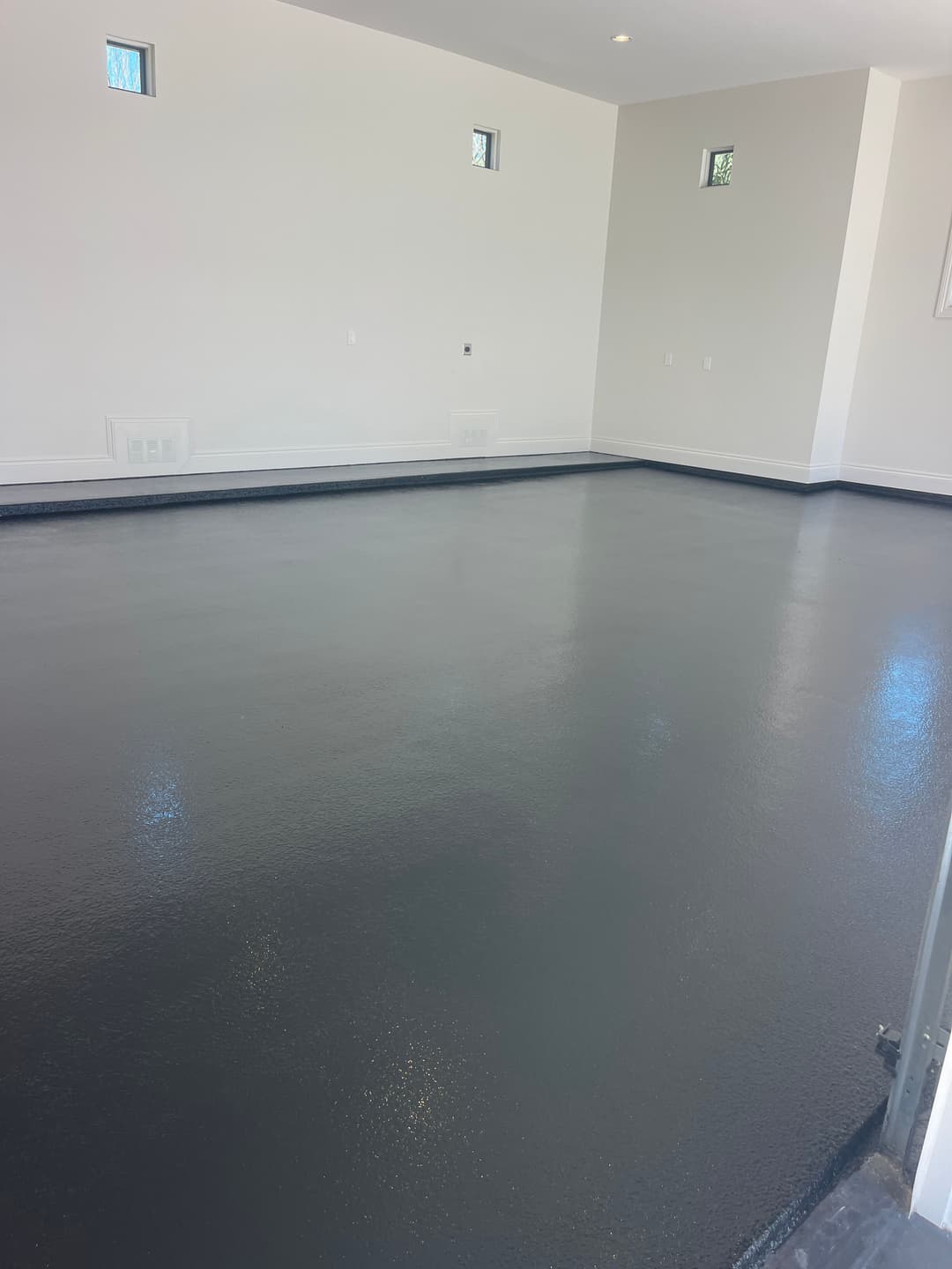 Newly coated gray epoxy floor in a bright, empty room with white walls and small windows.