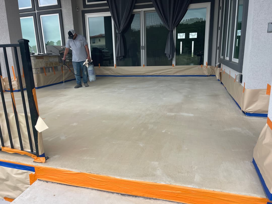 Man applying sealant on a recently prepared concrete porch with protective tape around edges.