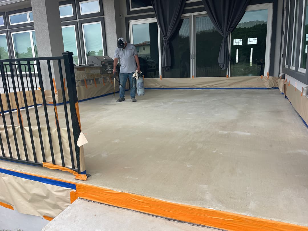 Worker applying finish to a newly poured concrete patio, surrounded by protective coverings.