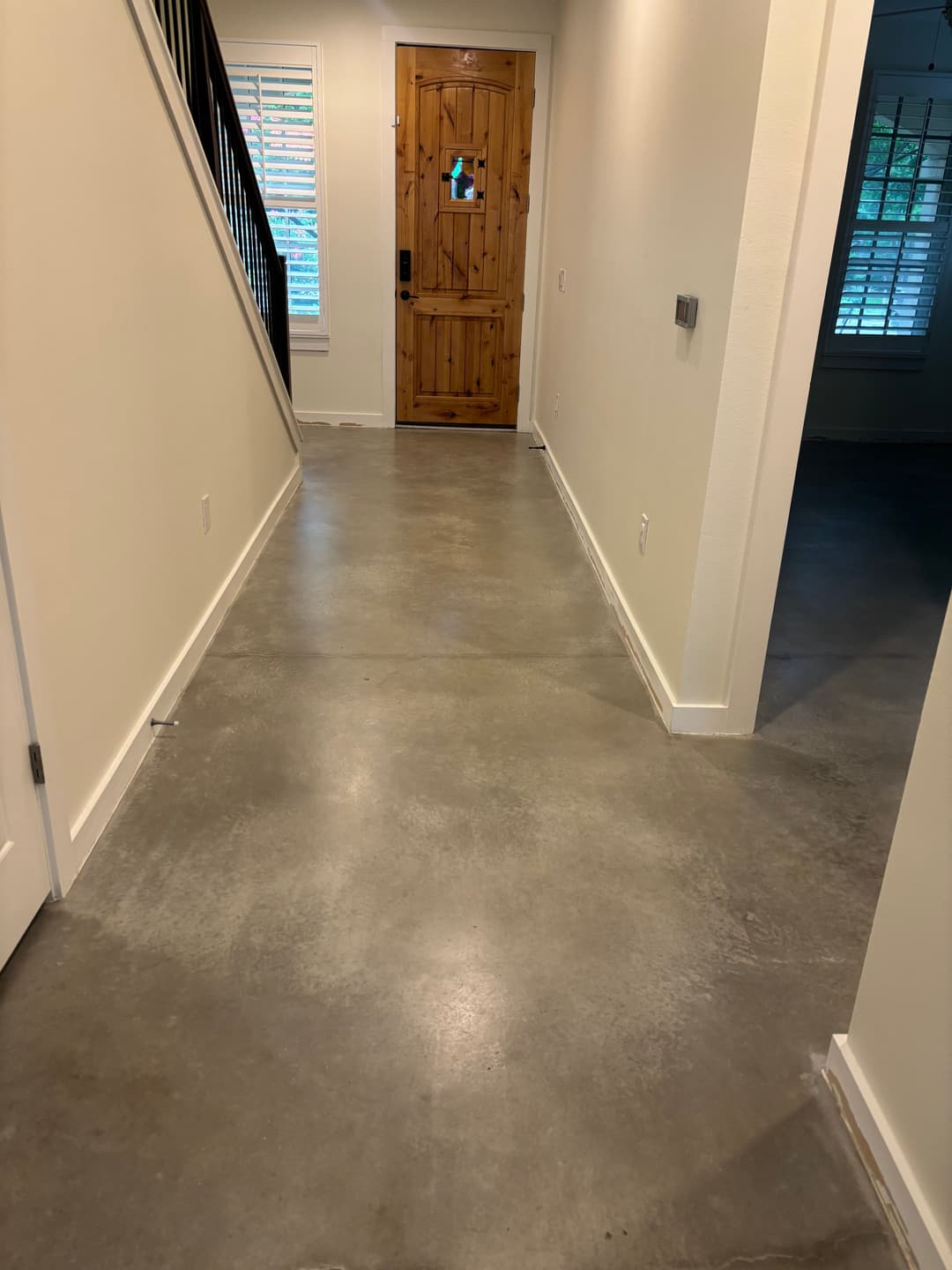 Concrete hallway leading to a wooden front door, bright natural light streaming in.