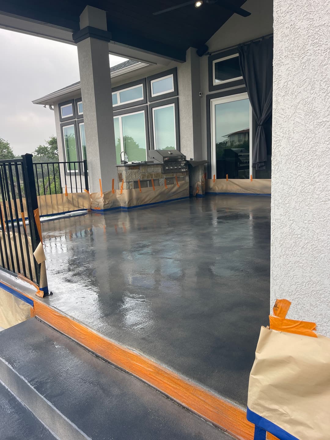 Newly sealed outdoor patio with modern grill, protective tape, and sleek concrete finish.