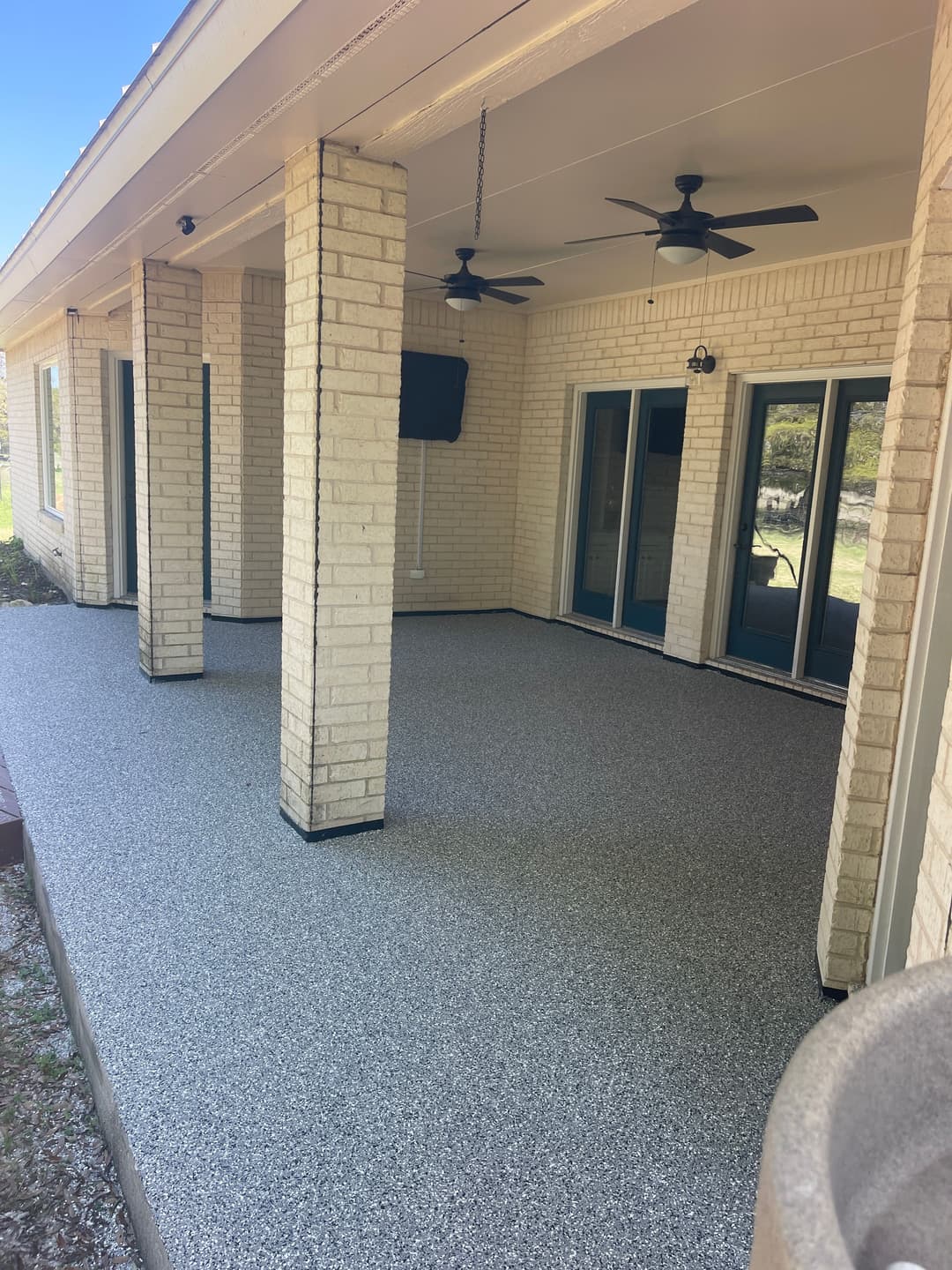 Spacious covered patio with light-colored brick columns and textured flooring.