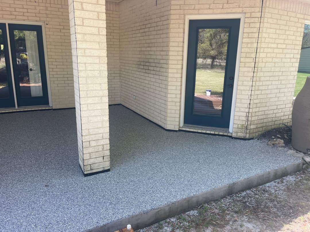 Covered patio with new textured flooring, brick walls, and glass doors leading outside.