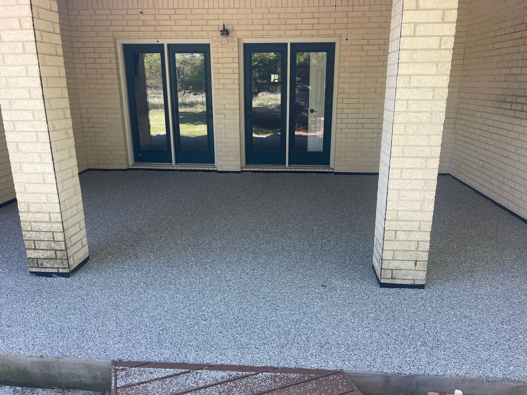 Covered patio with a textured floor and double glass doors, framed by brick columns.