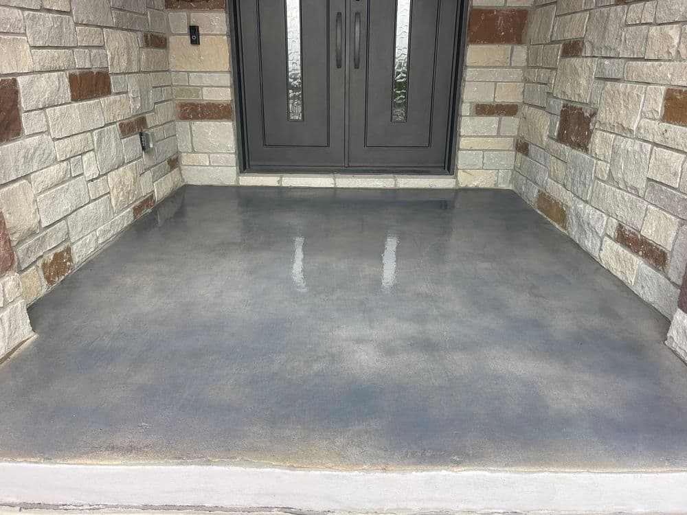 Newly poured concrete porch with decorative stone accents and double front doors.